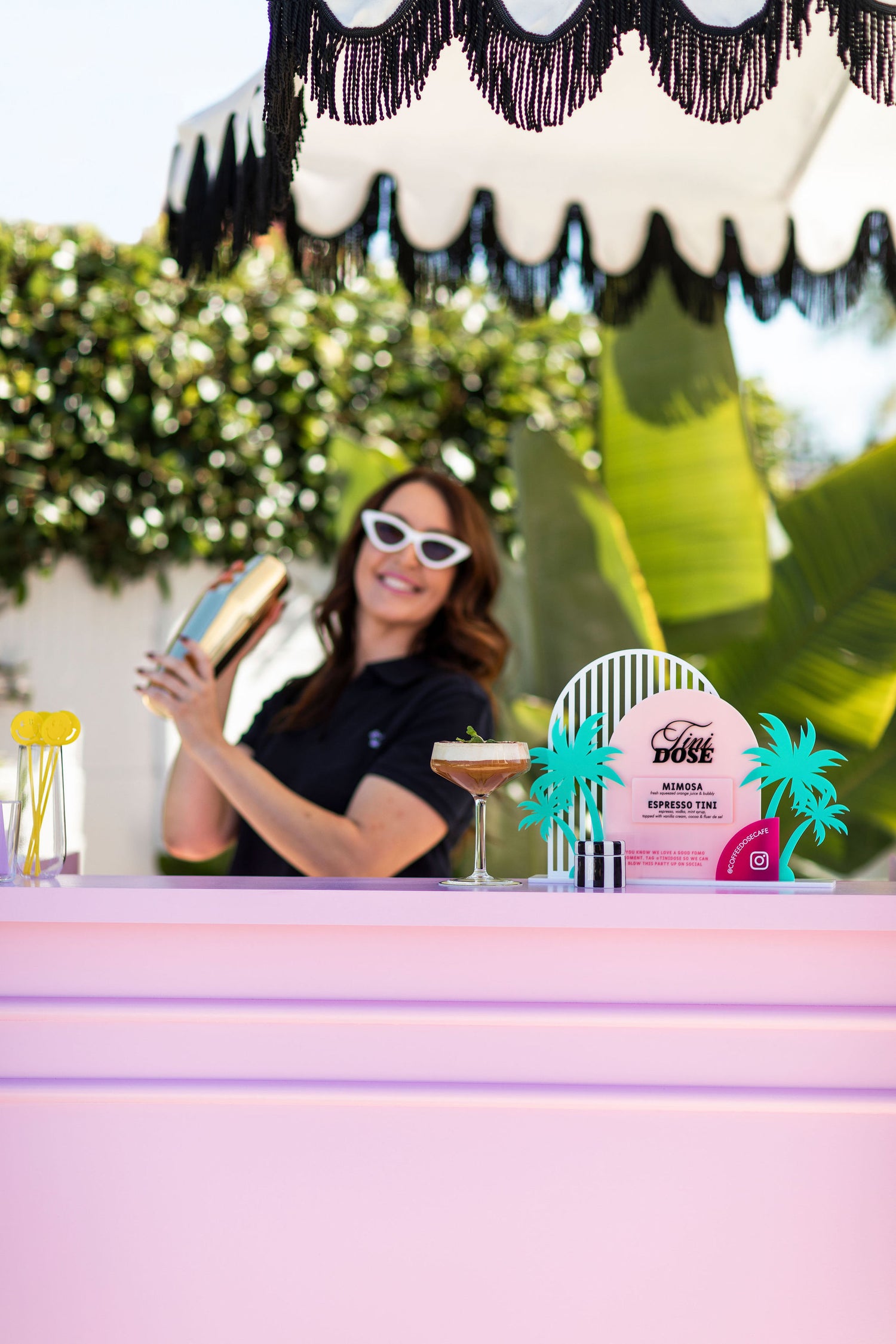cocktail on bar with tini dose paradise sign in focus with dose dealer in background shaking up a new drink