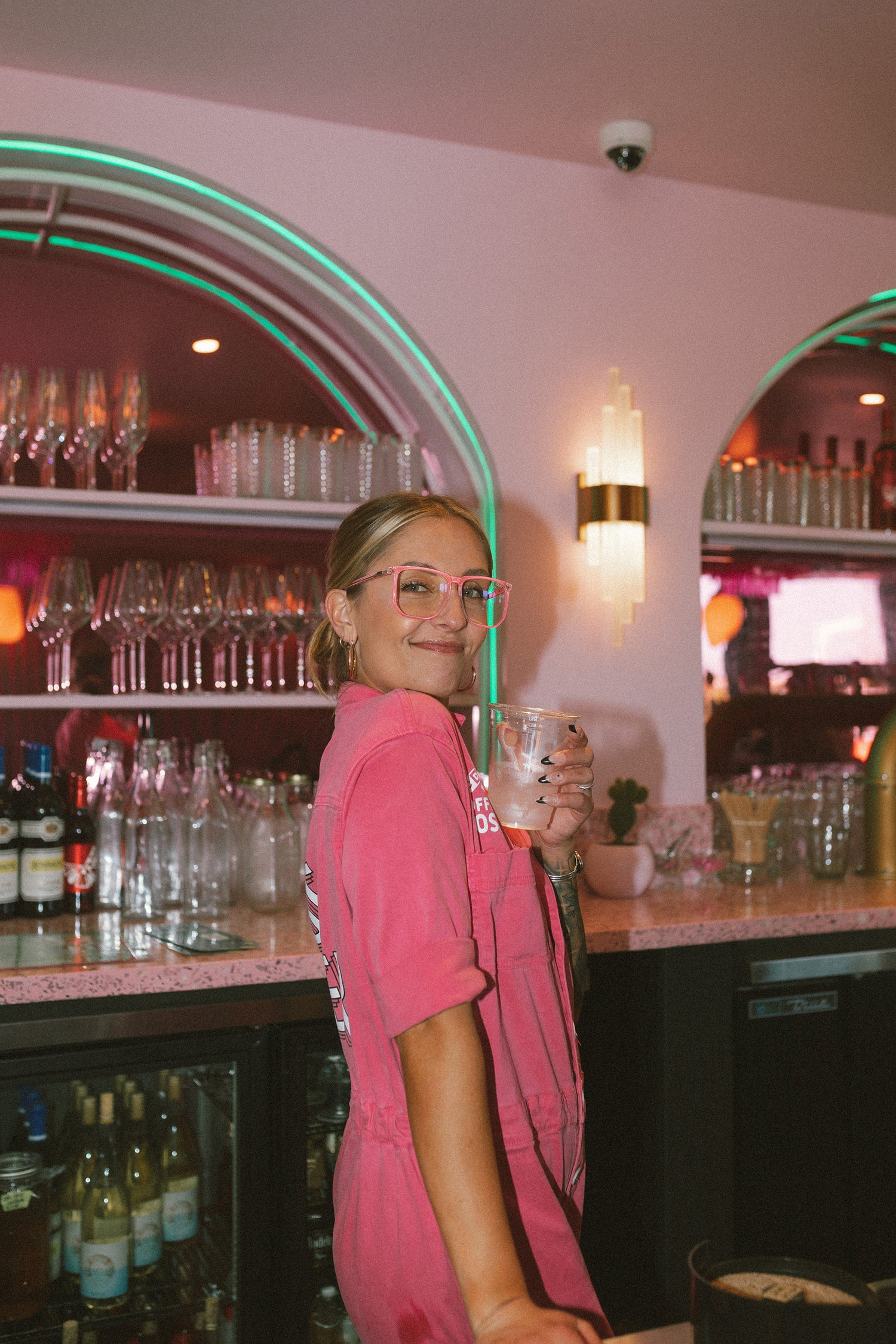 vibe dealer in pink jumpsuit having a good time holding drink up
