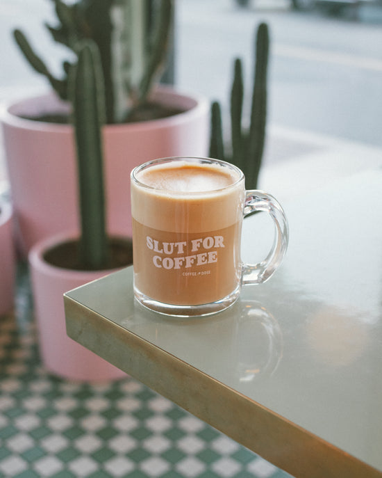 latte drink in a glass mug sitting on the corner of a coffee shop table with