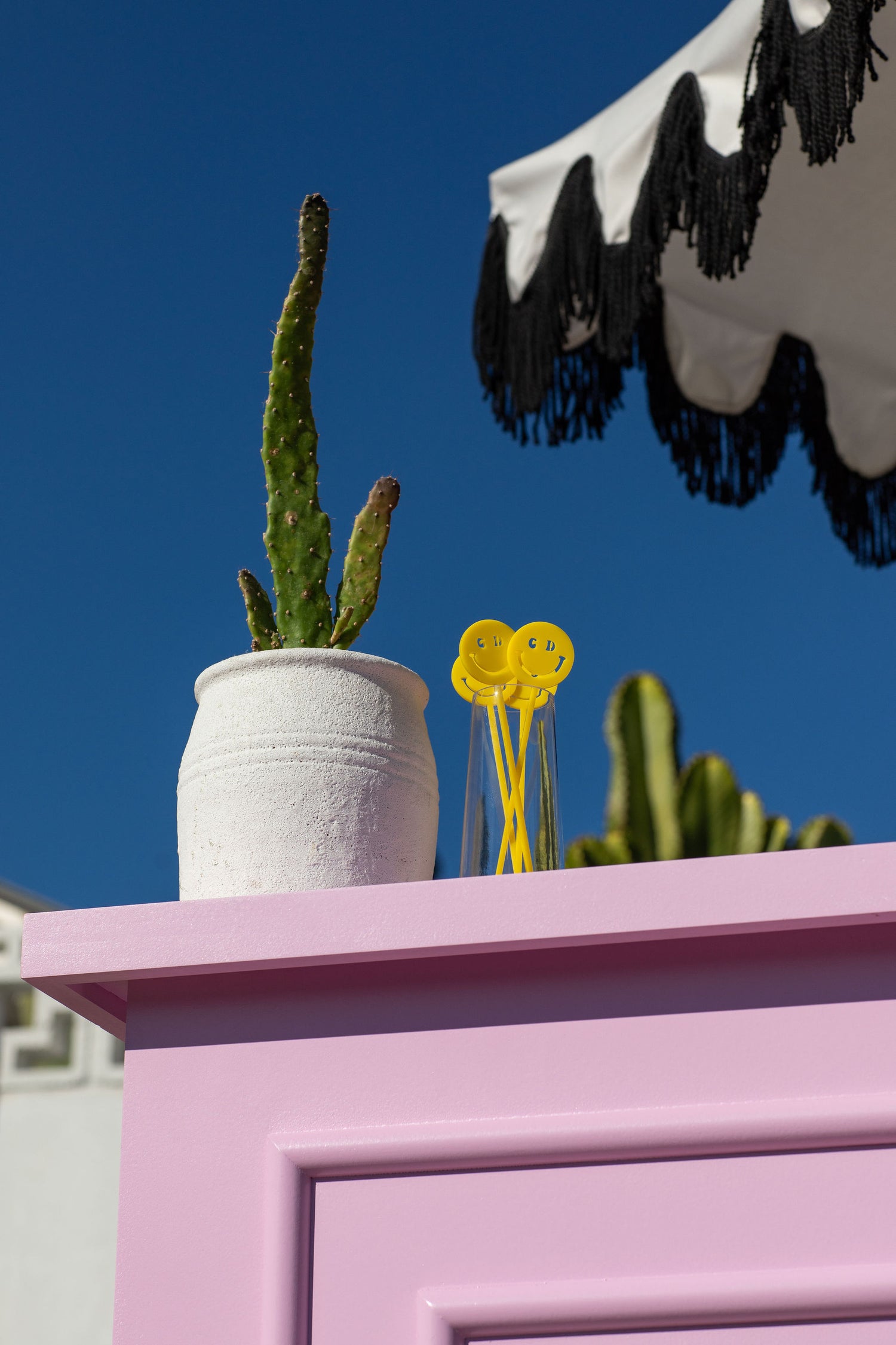 yellow smiley cocktail picks in glass holder on edge of pink bar, with small cactus plant nearby