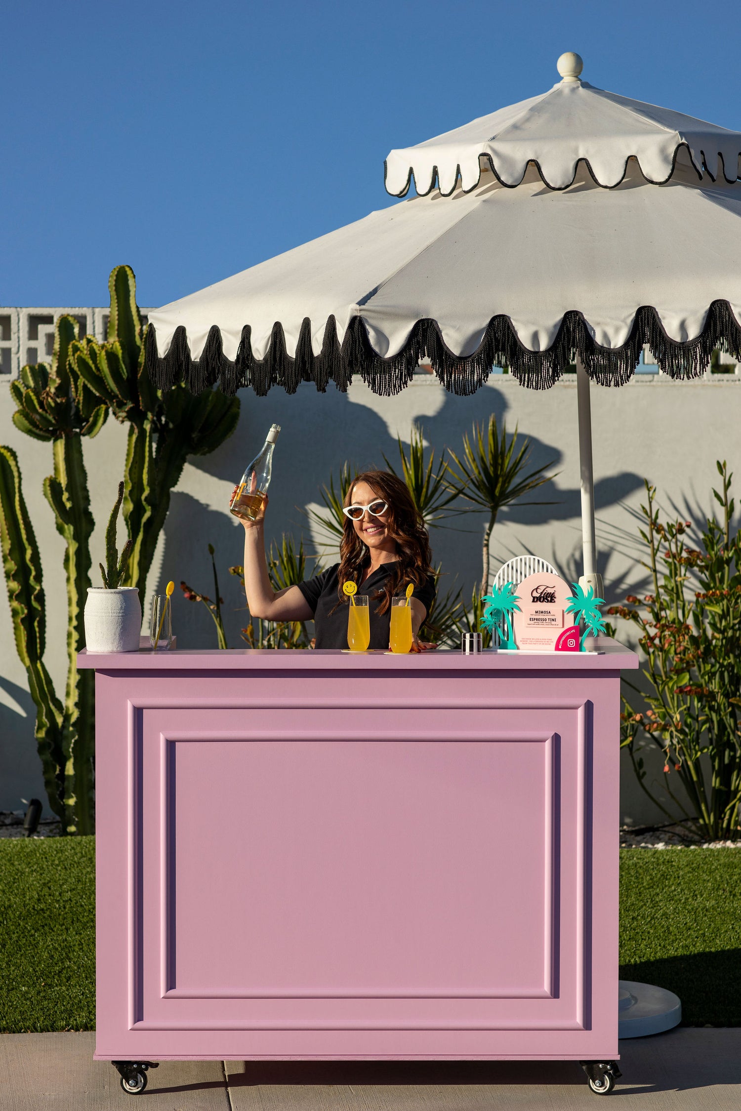 cute pink bar with white umbrella, dose dealer holding up drink has drinks prepared on bar ready to be consumed