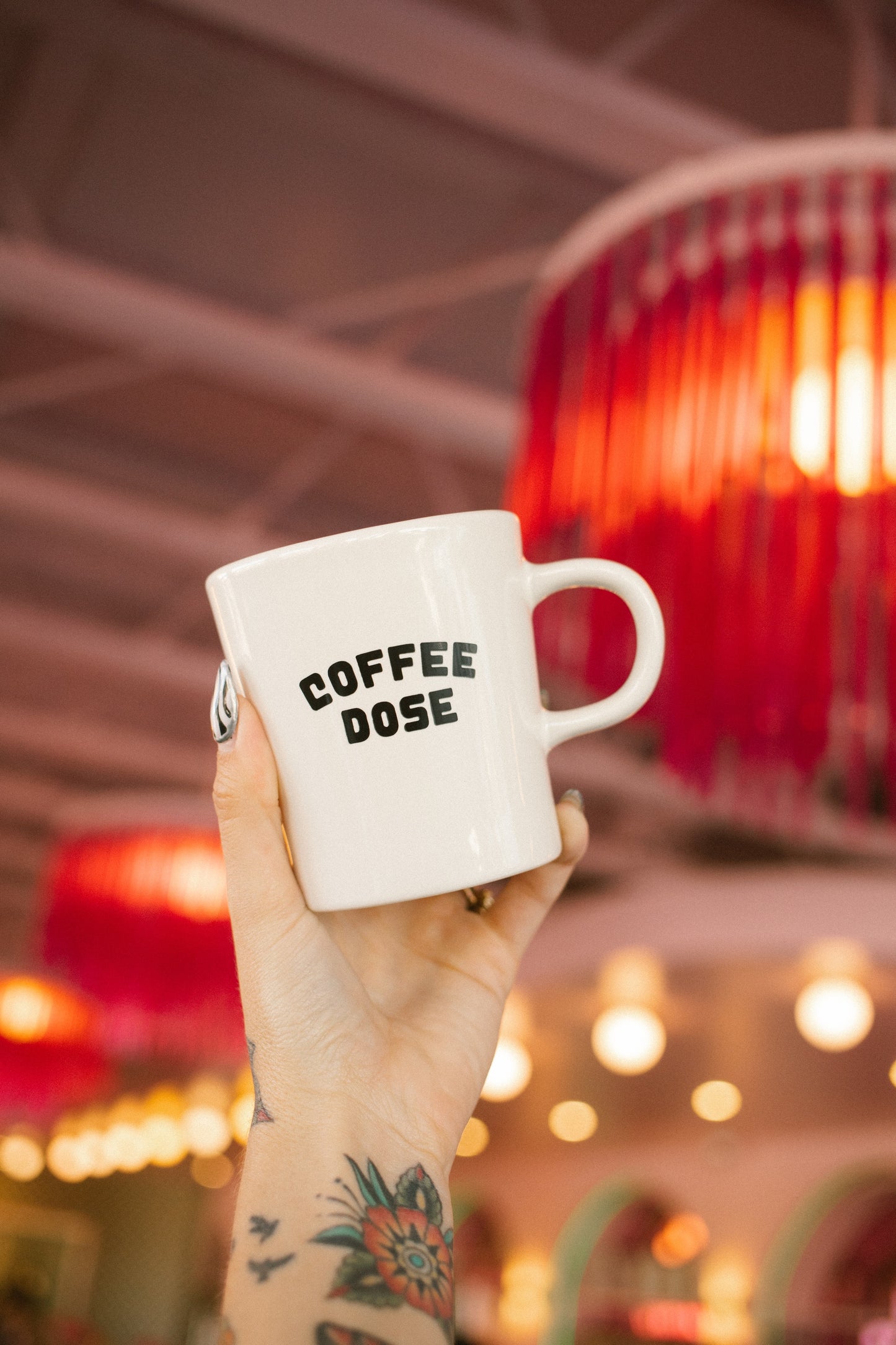 Hand holding a mug with 'COFFEE DOSE' text in a pink coffee shop.