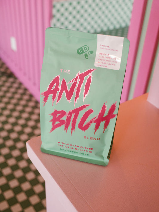 Coffee package labeled 'The Anti Bitch Blend' on a pink surface with a checkered pattern.