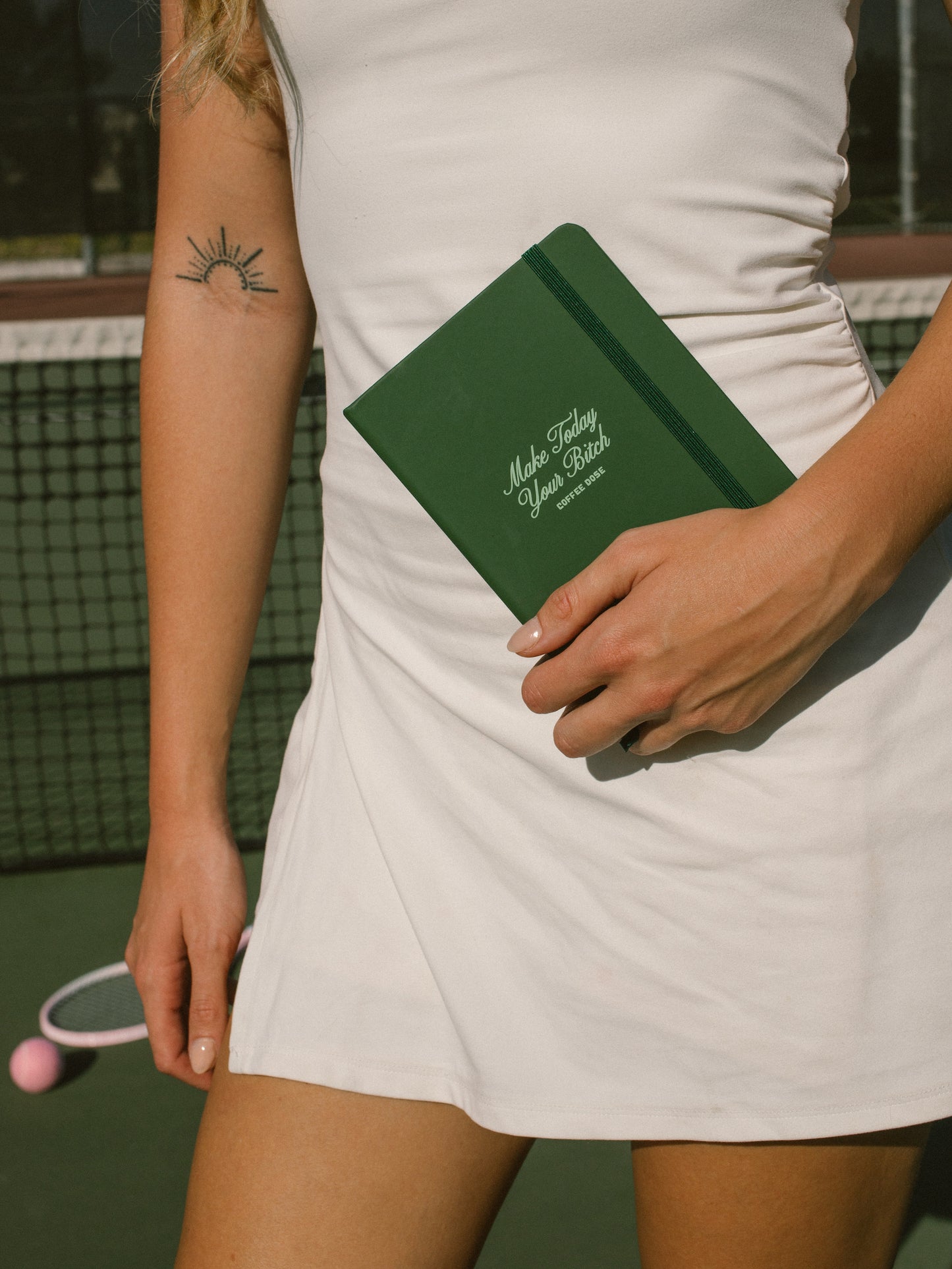 Person holding a green notebook that says 'make today your bitch' on a tennis court