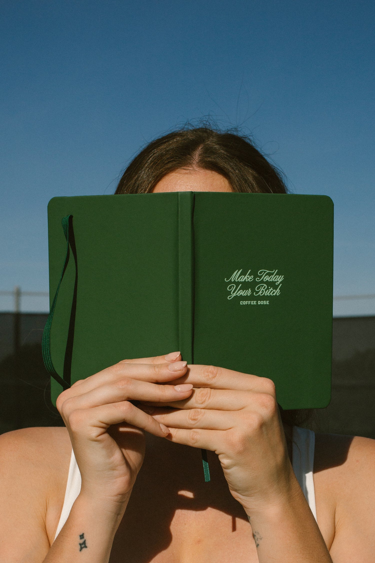 Person holding a green notebook with text that says 'make today your bitch' against a clear blue sky