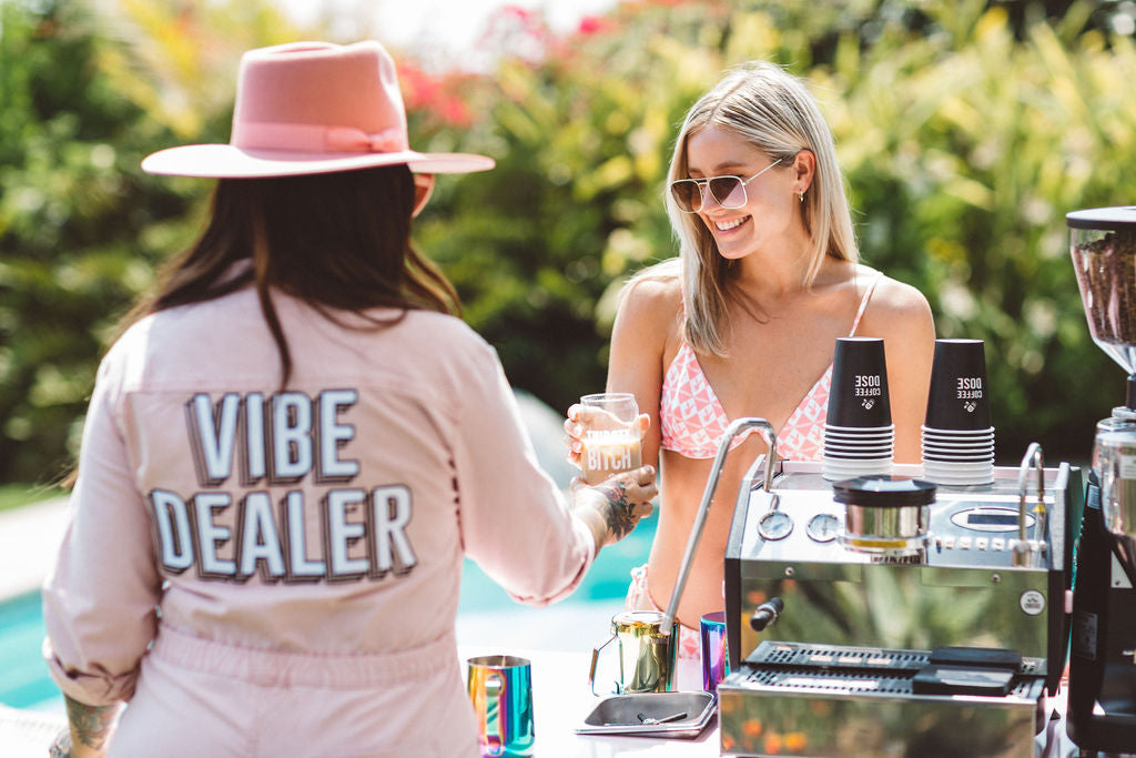 vibe dealer in pink jumpsuit handing an iced coffee drink to a pool party goer