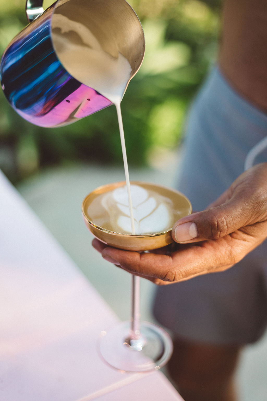 pouring the steamed milk into a martini like glass with a latte drink, forming a leaf like shape