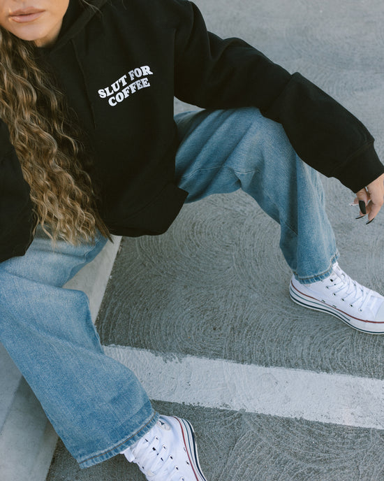 relaxing in a parking lot on parking bumper in black hoodie with white text 